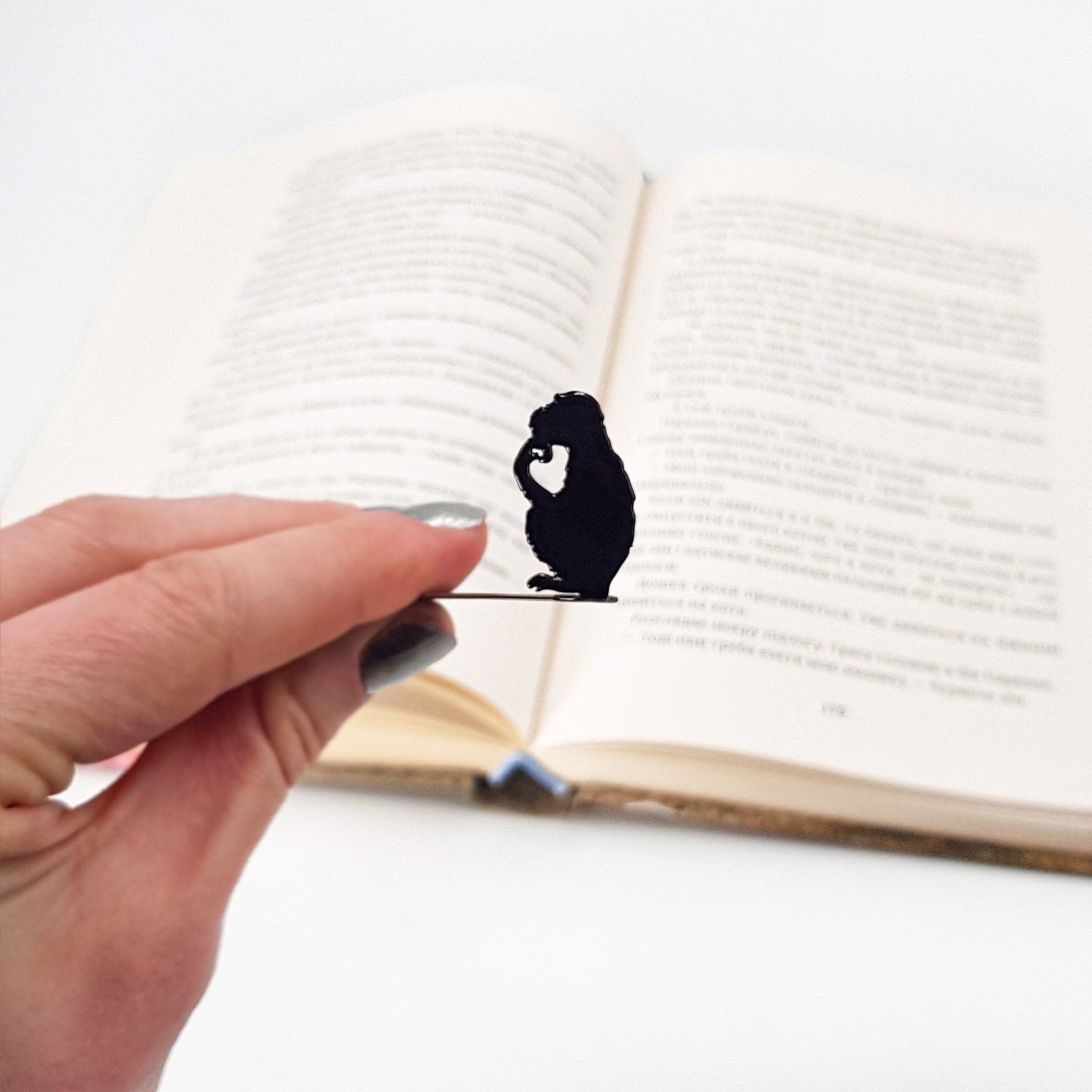 Monkey the Thinker metal bookmark held up beside an open book