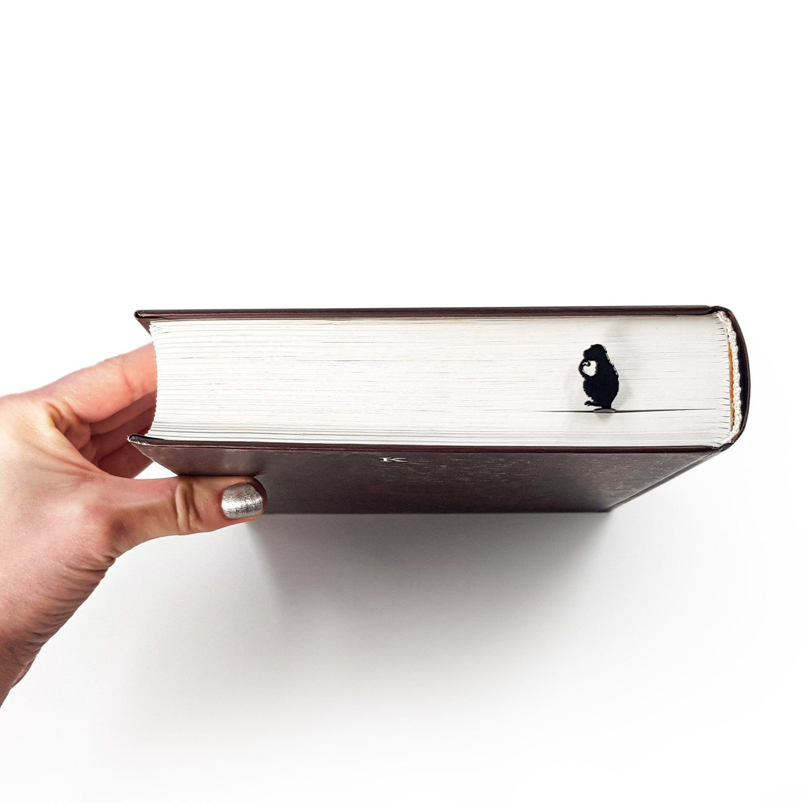 Monkey the Thinker metal bookmark held in a hand above an open book