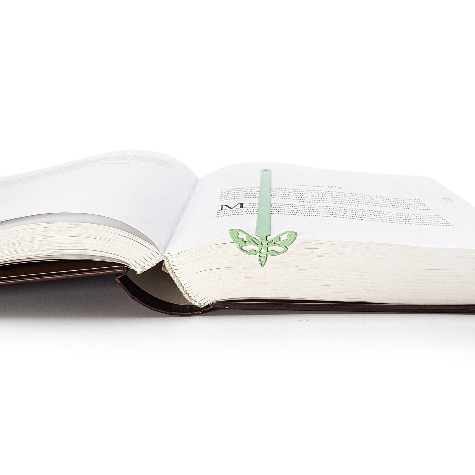 Moth metal bookmark in green marking a page in an open book