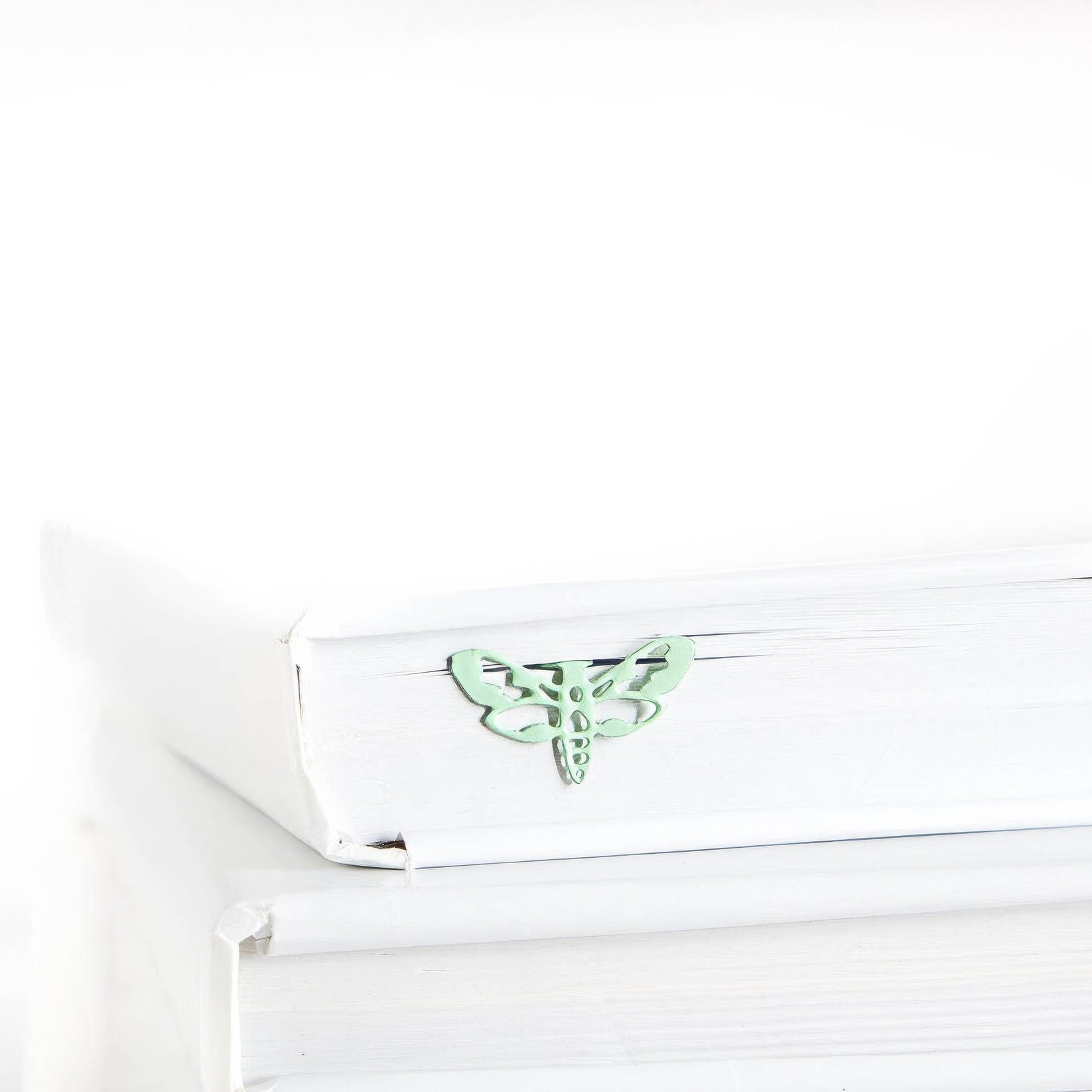 Moth metal bookmark in green in a closed book, only its top showing above the pages