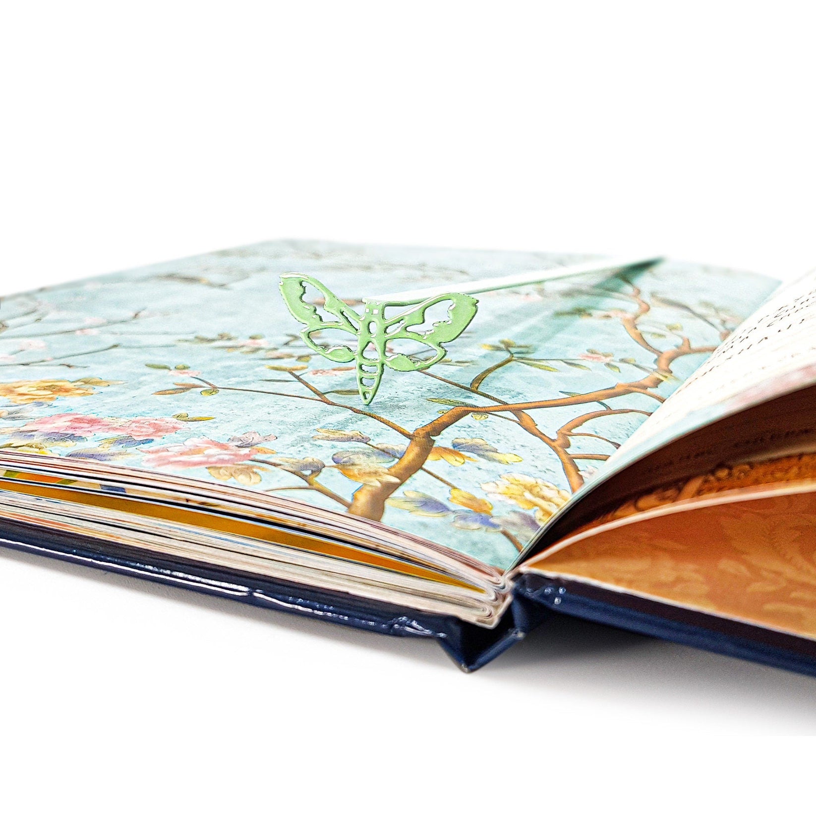Moth metal bookmark in green marking a page in an illustrated book