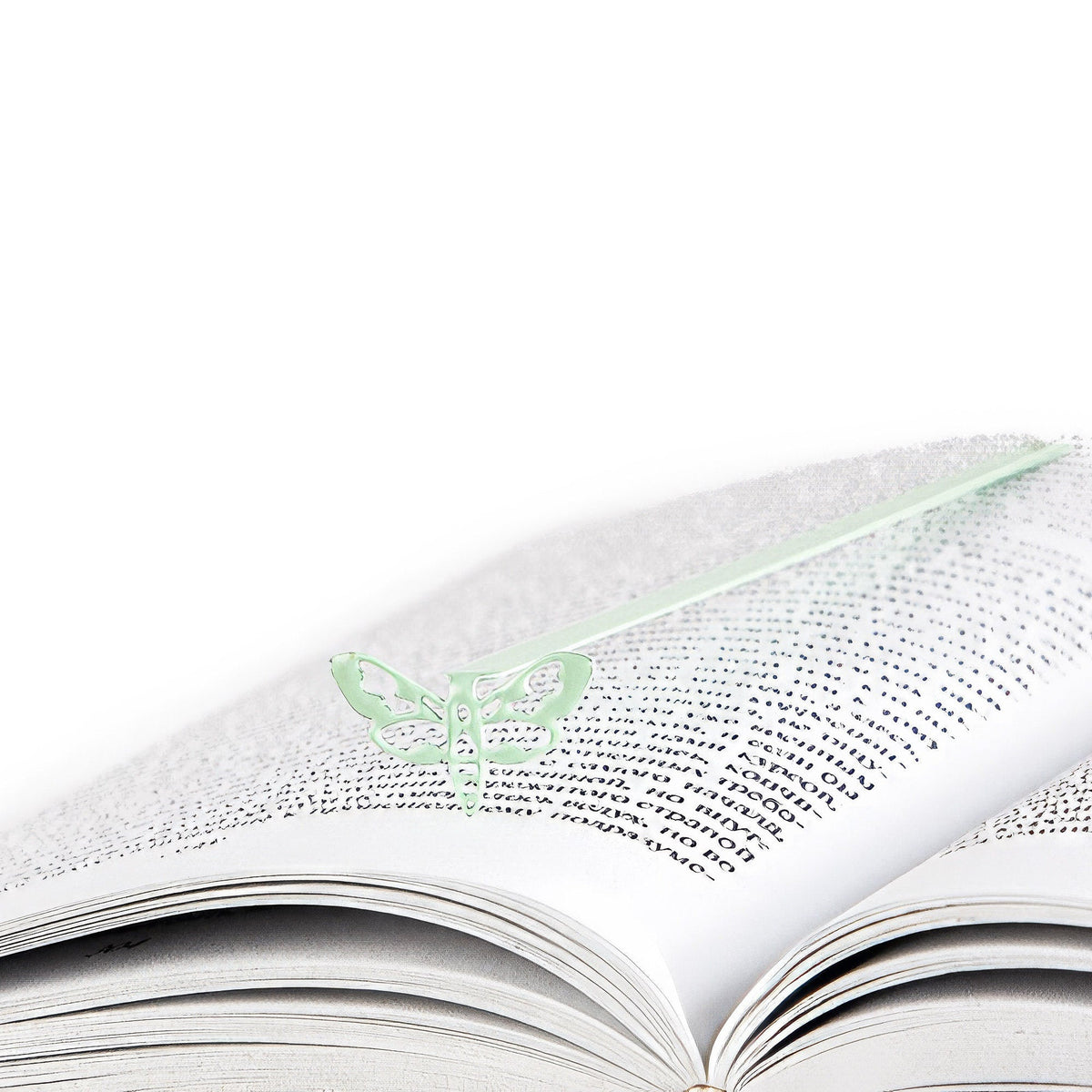 Moth metal bookmark in green lying across the pages of an open book
