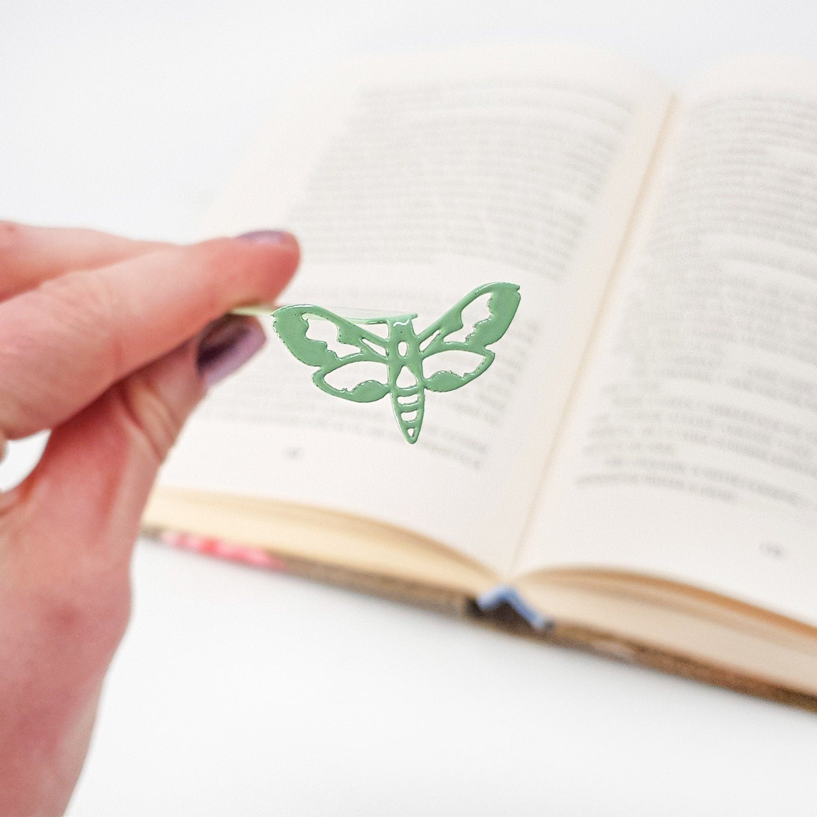 Moth metal bookmark in green held in a hand above an open book