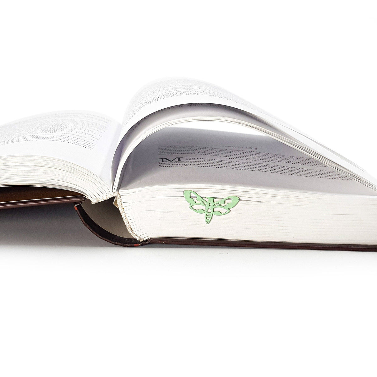 Moth metal bookmark in green resting on the pages of an open book