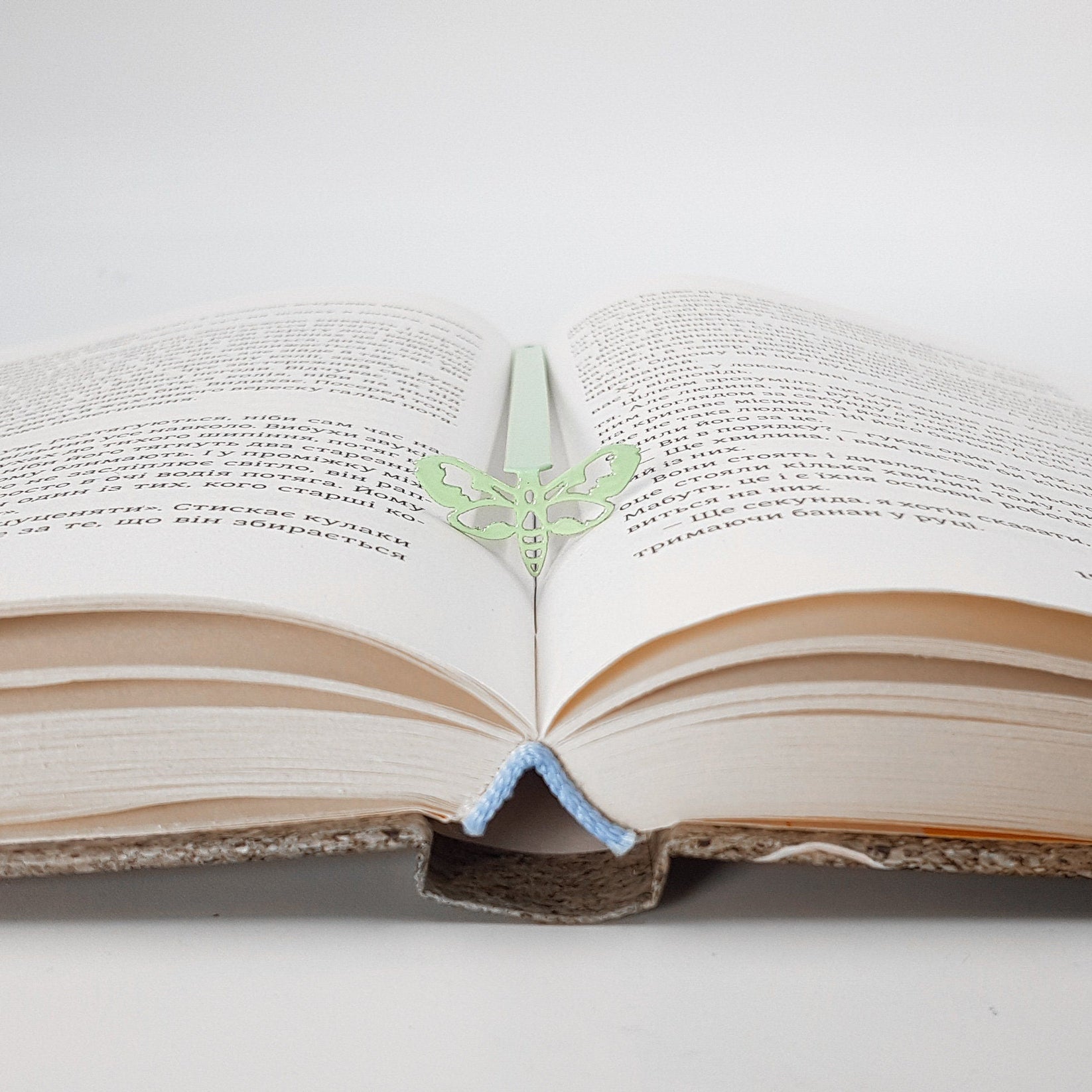Moth metal bookmark in green set into the gutter of an open book