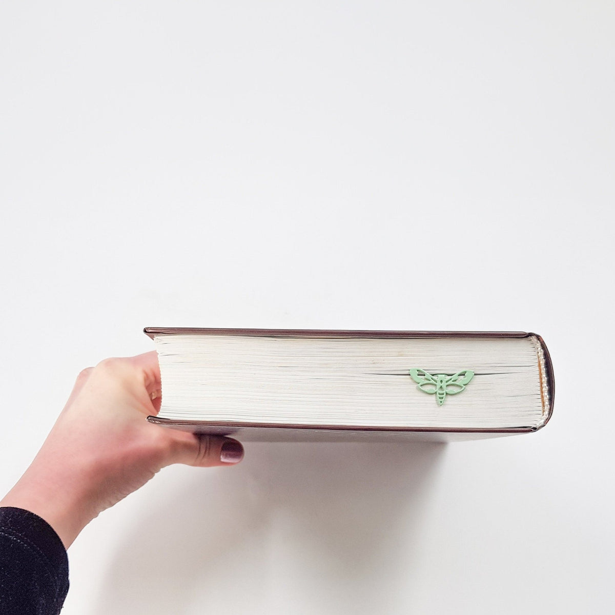 Moth metal bookmark in green held in a hand to show its size