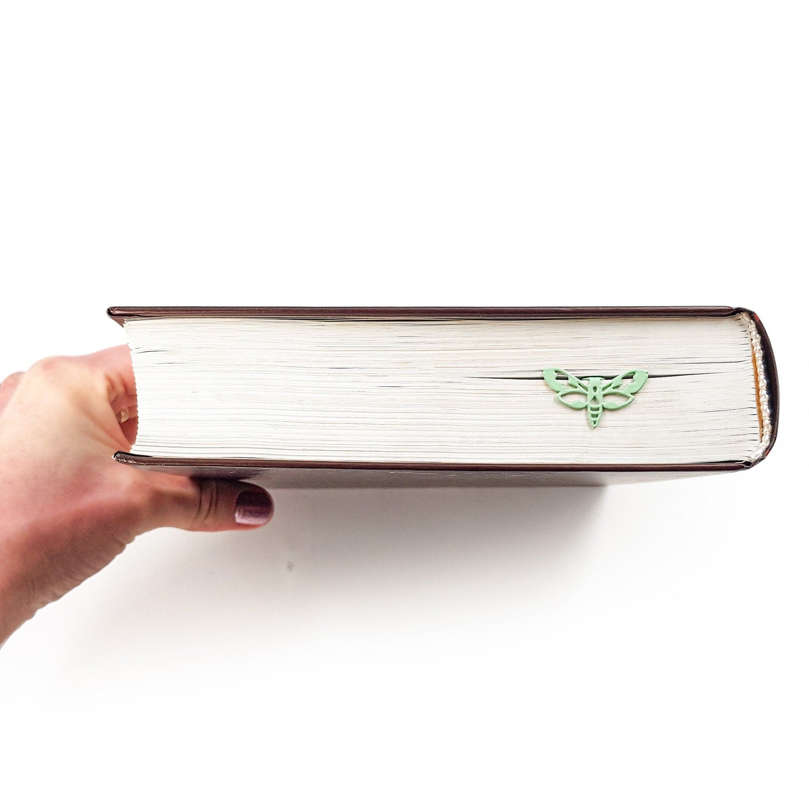 Moth metal bookmark in green held up beside an open book