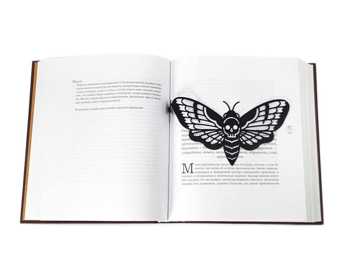 Moth of Death metal bookmark lying across the pages of an open book