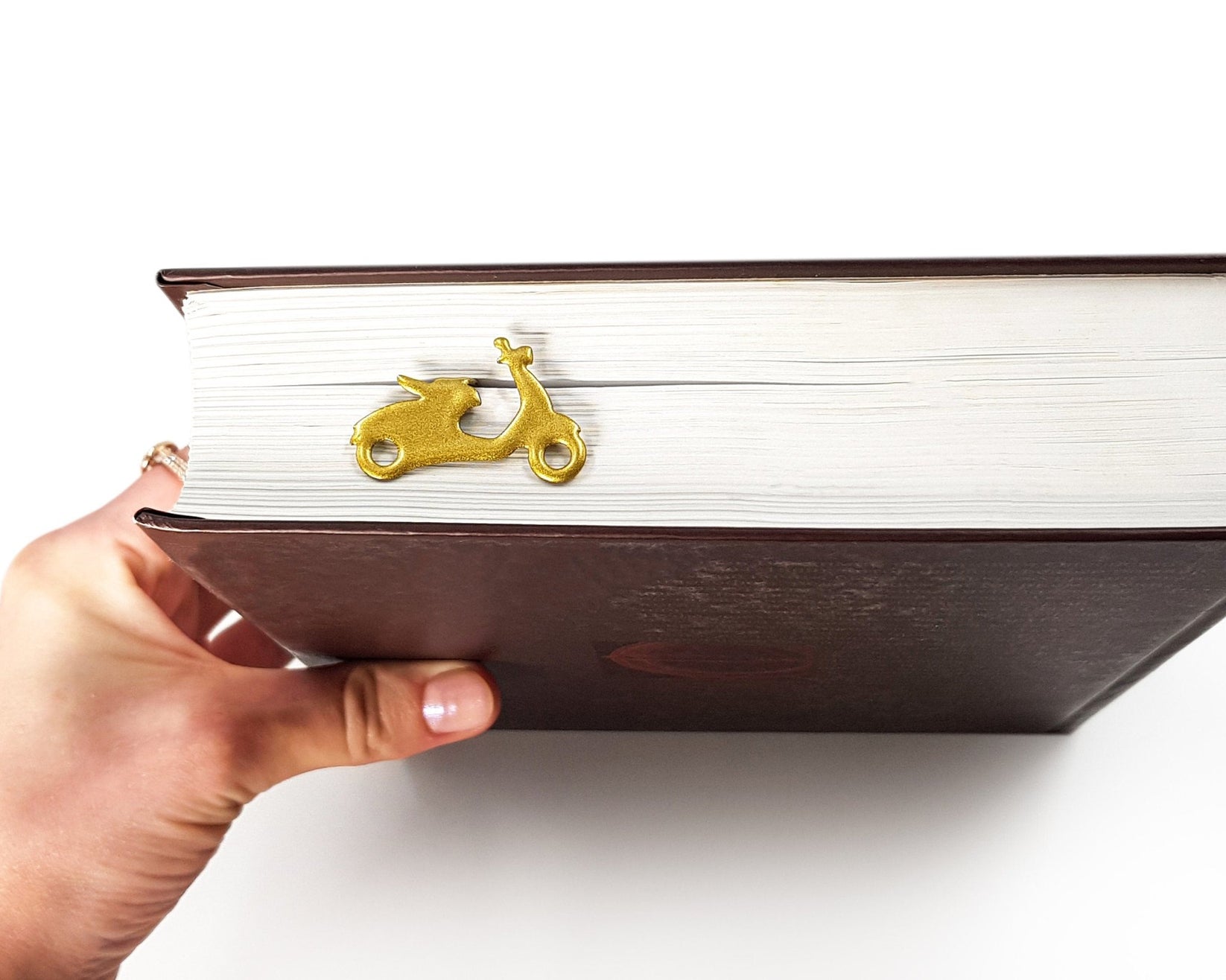 Motor Scooter metal bookmark in gold held up beside an open book