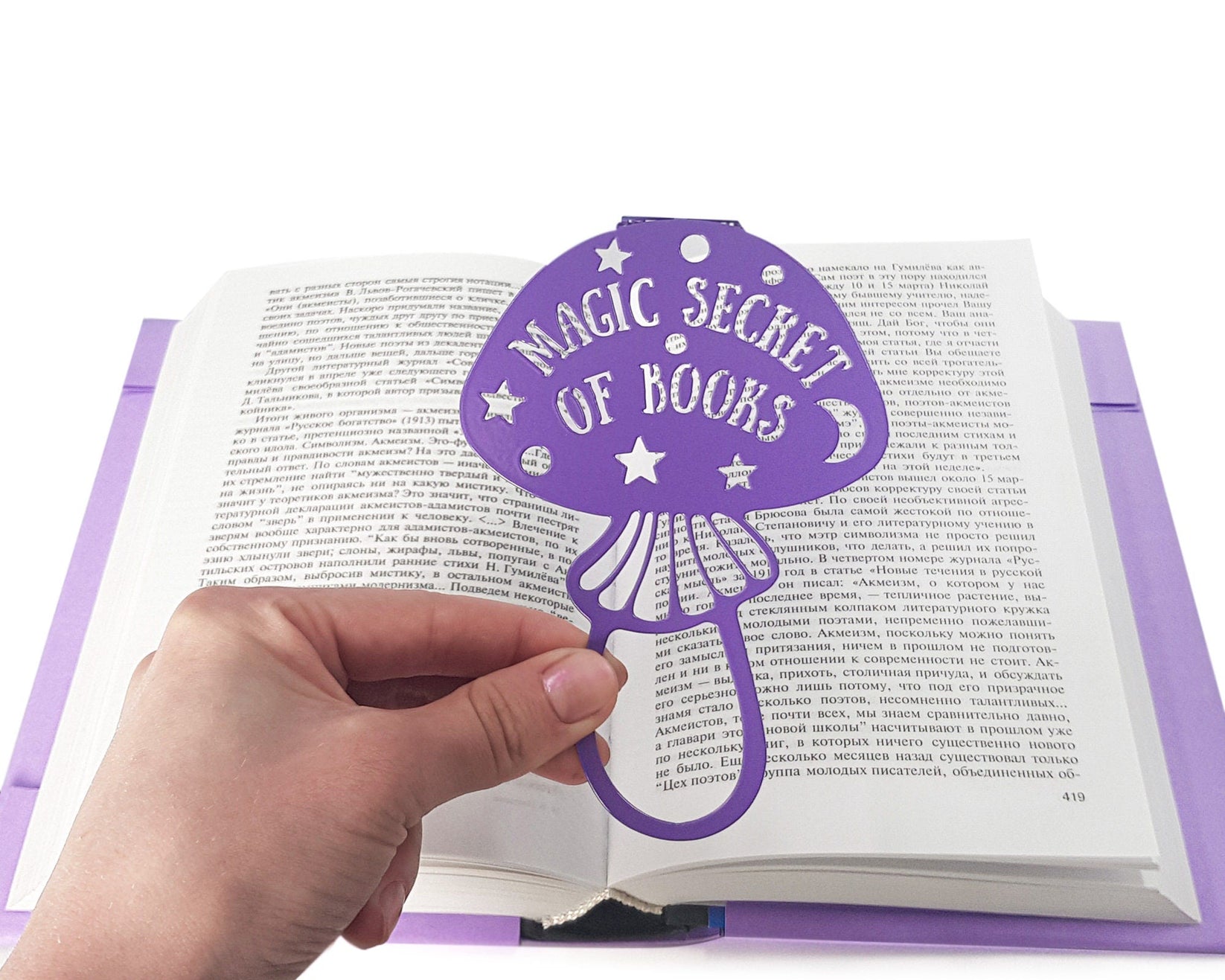 Mushroom metal bookmark in blue held in a hand above an open book