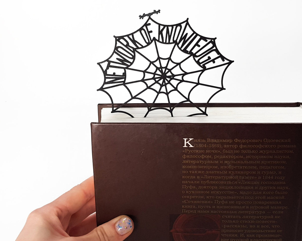Network of Knowledge metal bookmark held in a hand above an open book