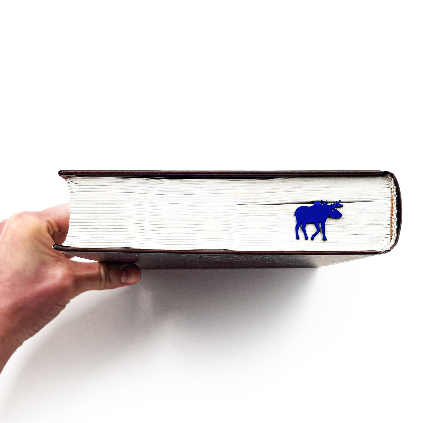 Norwegian Moose metal bookmark in blue held in a hand above an open book