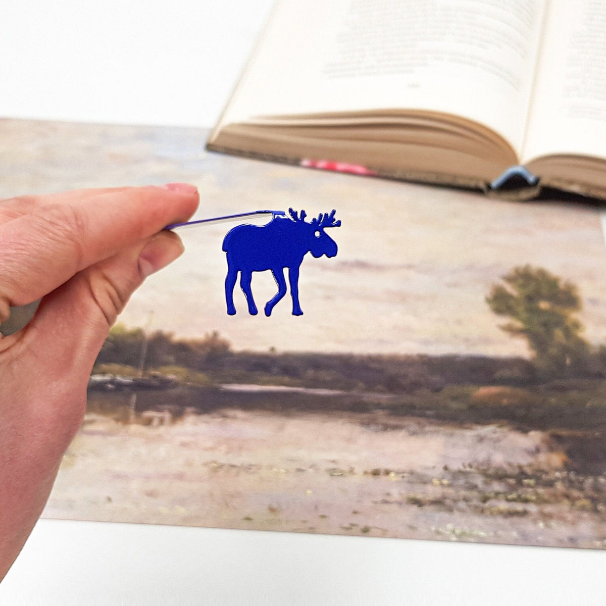 Norwegian Moose metal bookmark in blue marking a page in an illustrated book