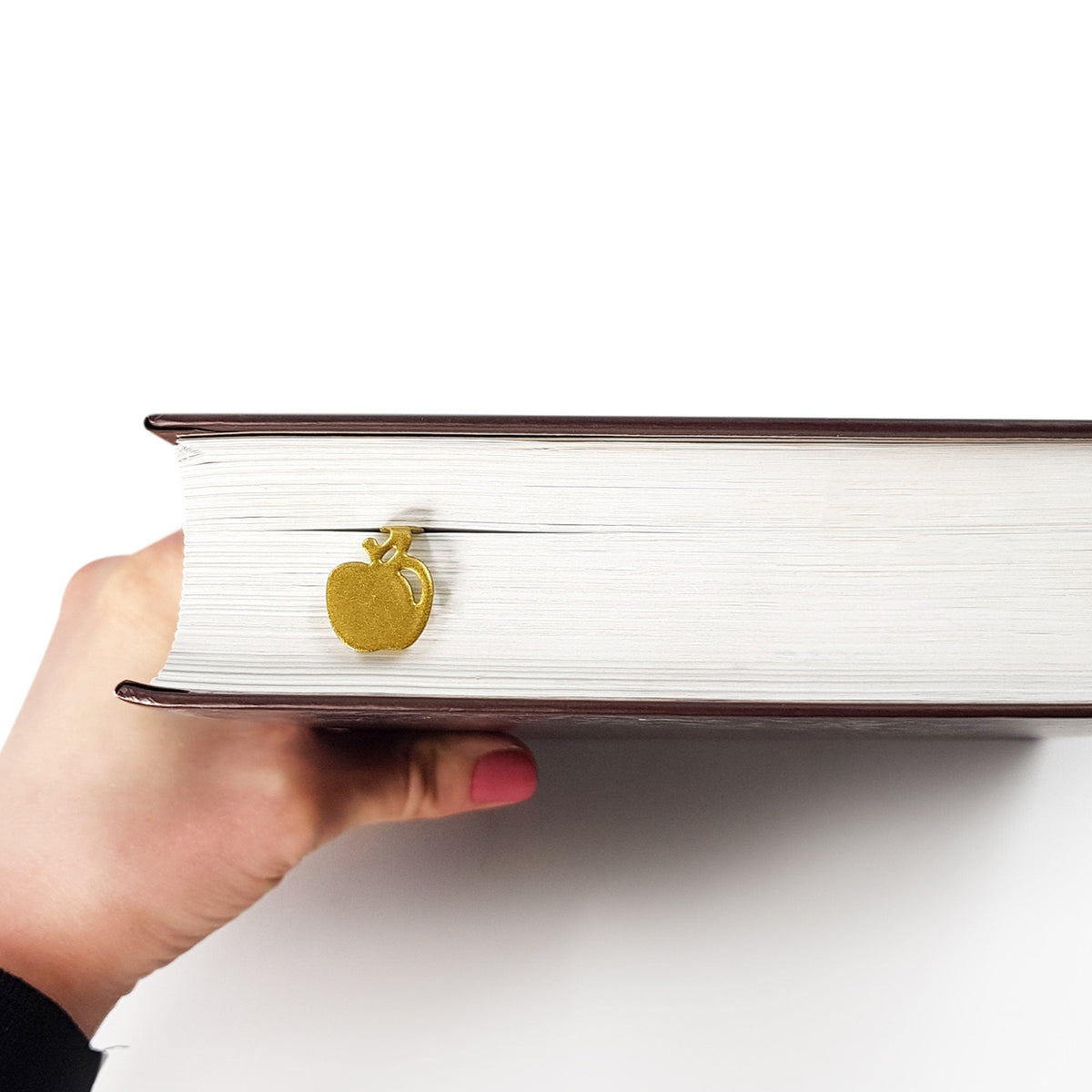 Paradise Apple' metal bookmark in gold held in a hand to show its size