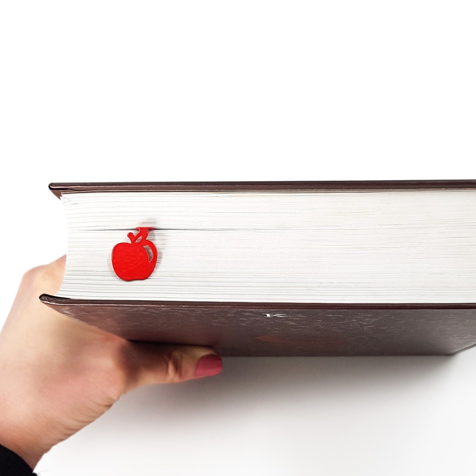 Paradise Apple' metal bookmark in red held in a hand above an open book