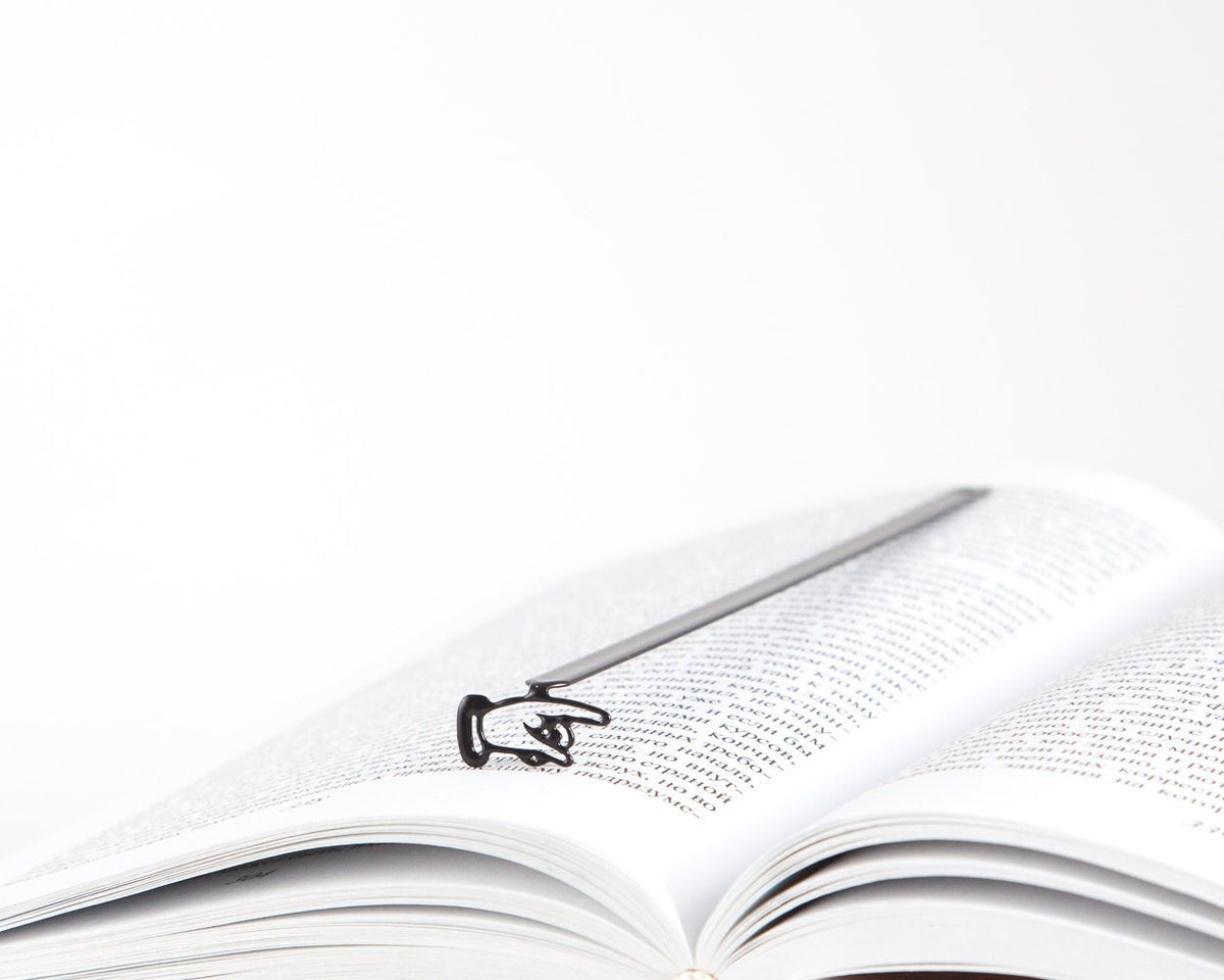 Pointing Finger metal bookmark resting on the pages of an open book
