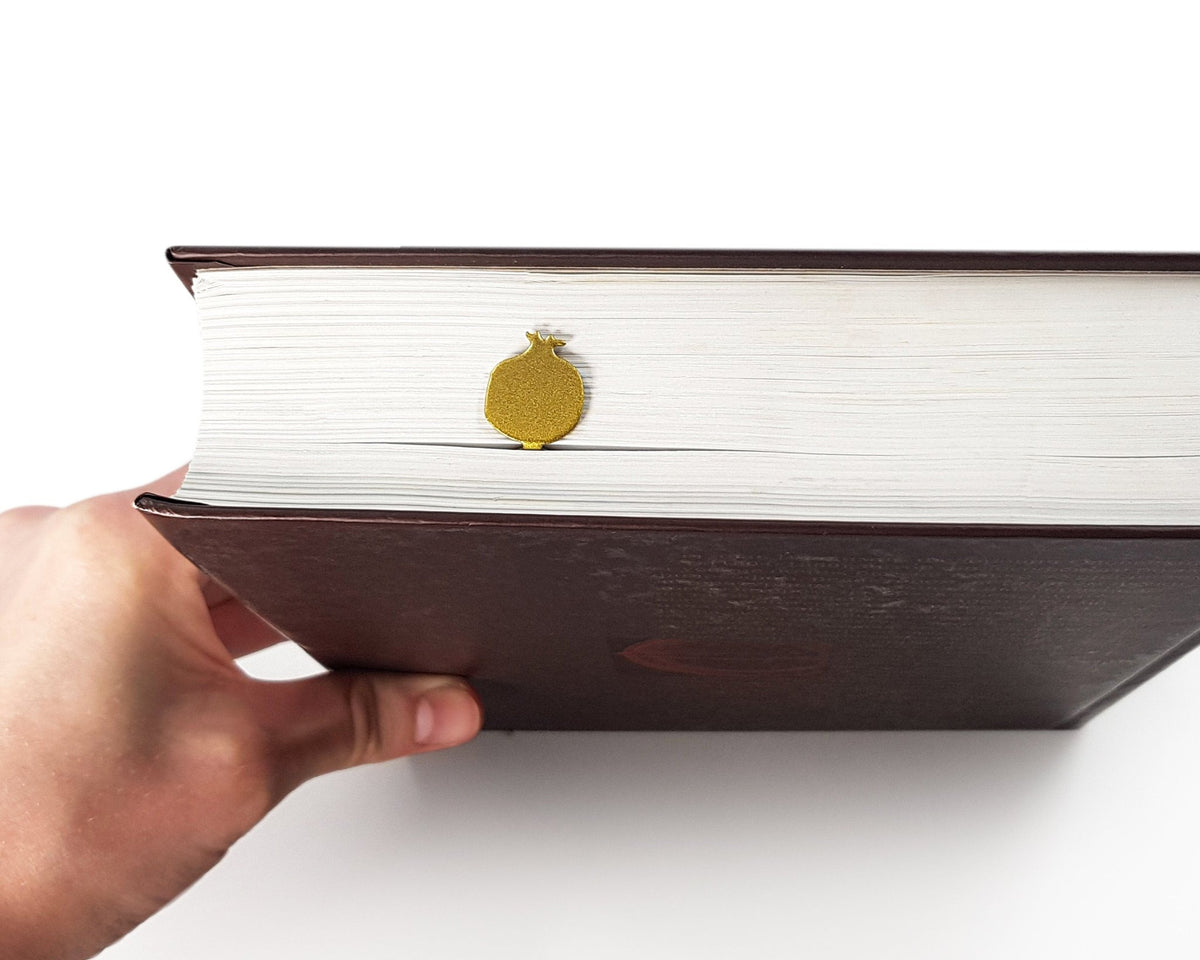 Pomegranate metal bookmark in gold seen from the edge of a closed book