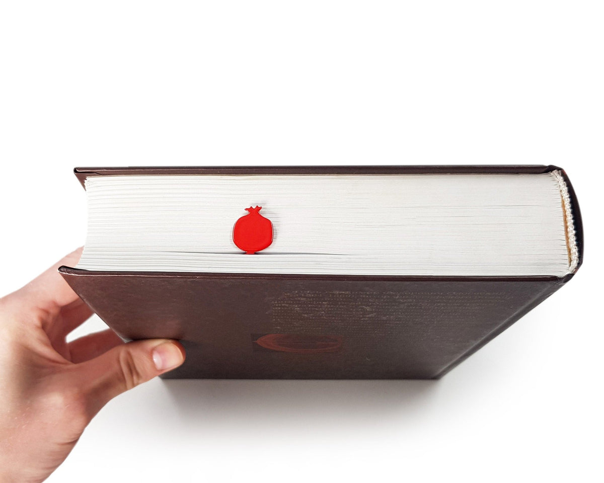Pomegranate metal bookmark in red in a closed book, only its top showing above the pages