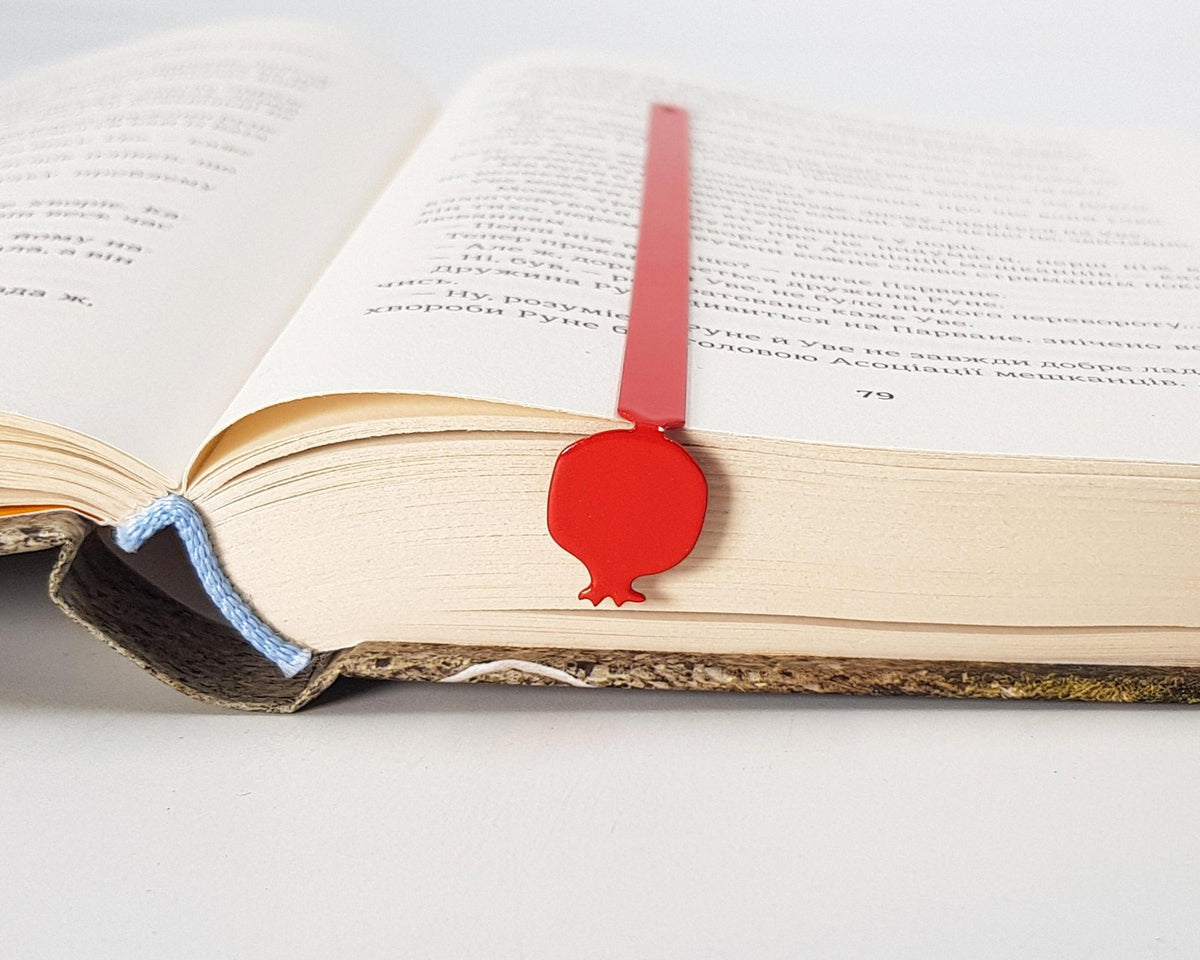 Pomegranate metal bookmark in red resting on the pages of an open book