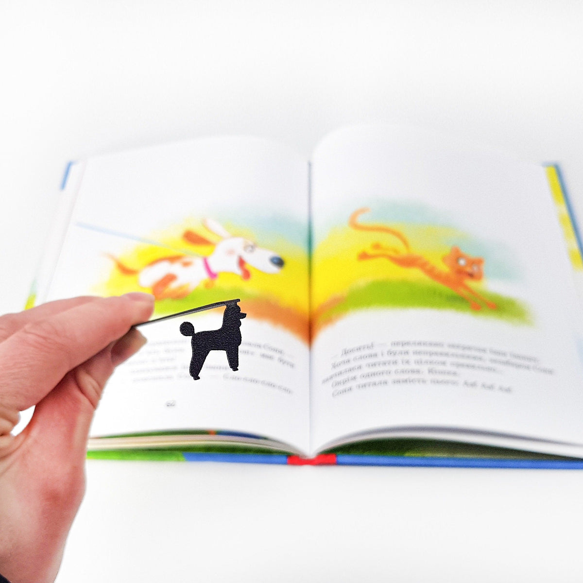 Poodle metal bookmark marking a page in an illustrated book