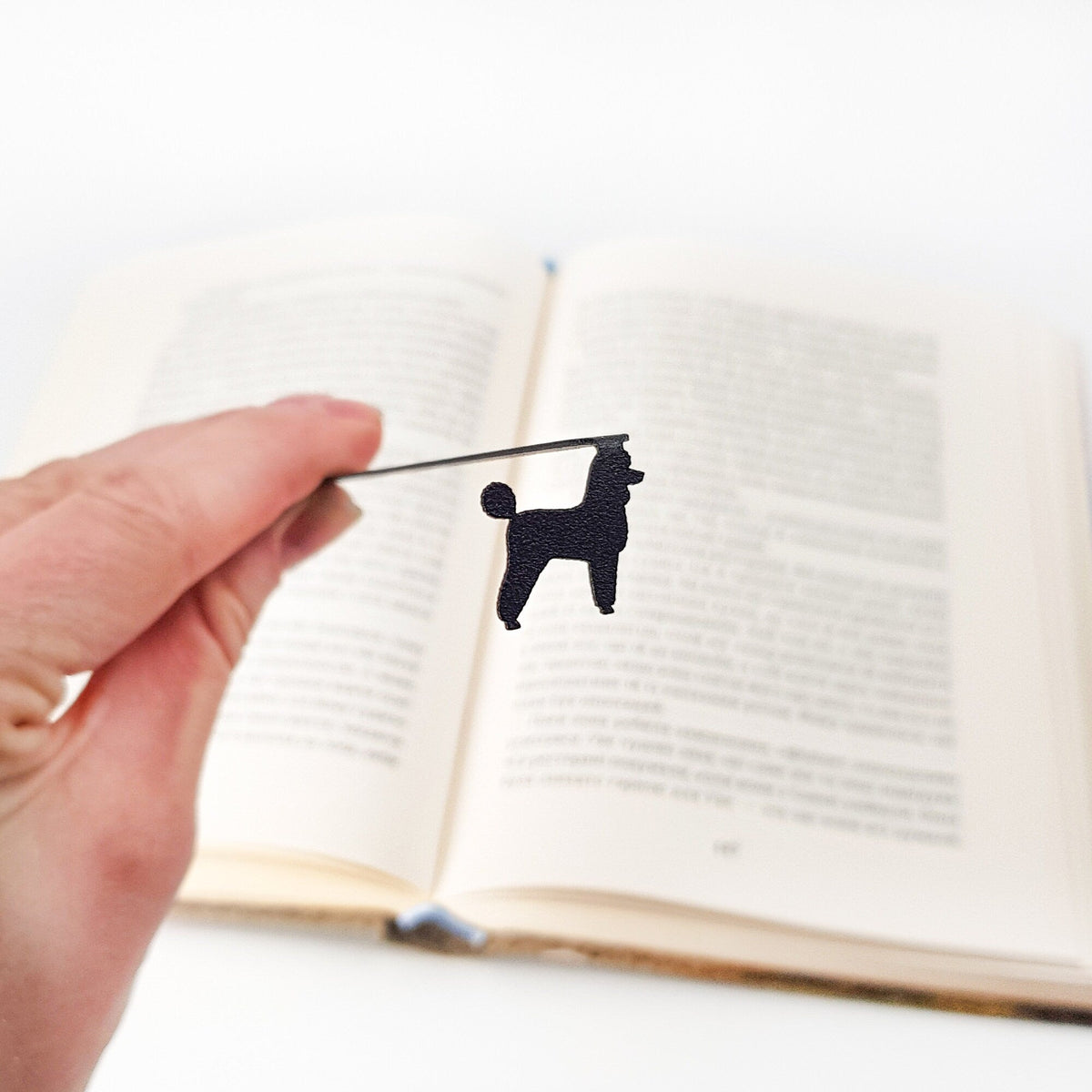 Poodle metal bookmark held up beside an open book