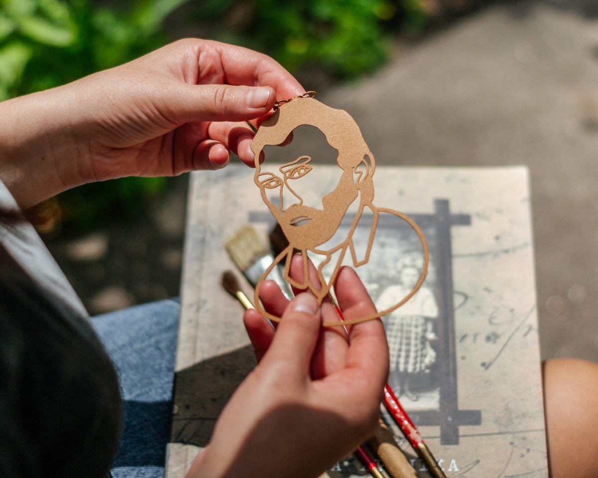 Van Gogh Portrait metal bookmark in gold held in a hand above an open book