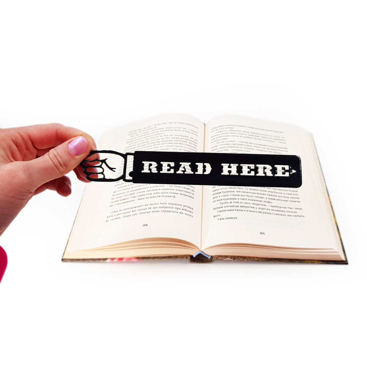 Read Here metal bookmark held up beside an open book