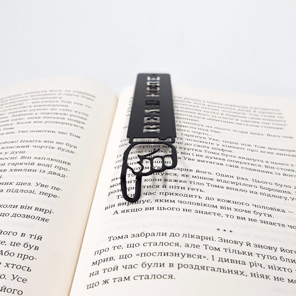 Read Here metal bookmark resting on the pages of an open book