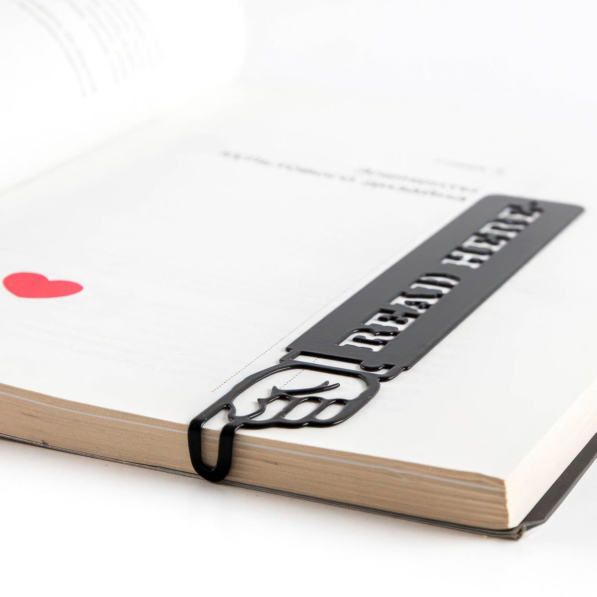 Read Here metal bookmark in a closed book, only its top showing above the pages