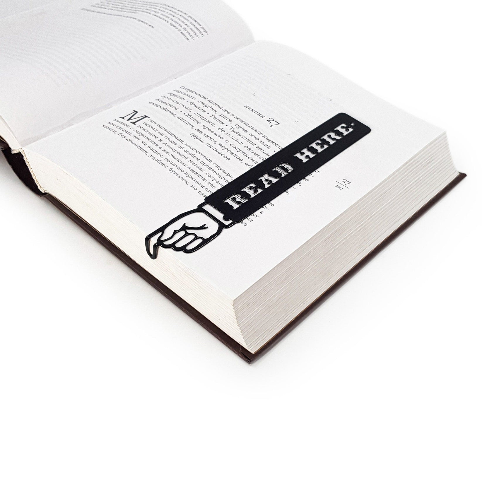 Read Here metal bookmark clipped in a closed book, viewed from the side