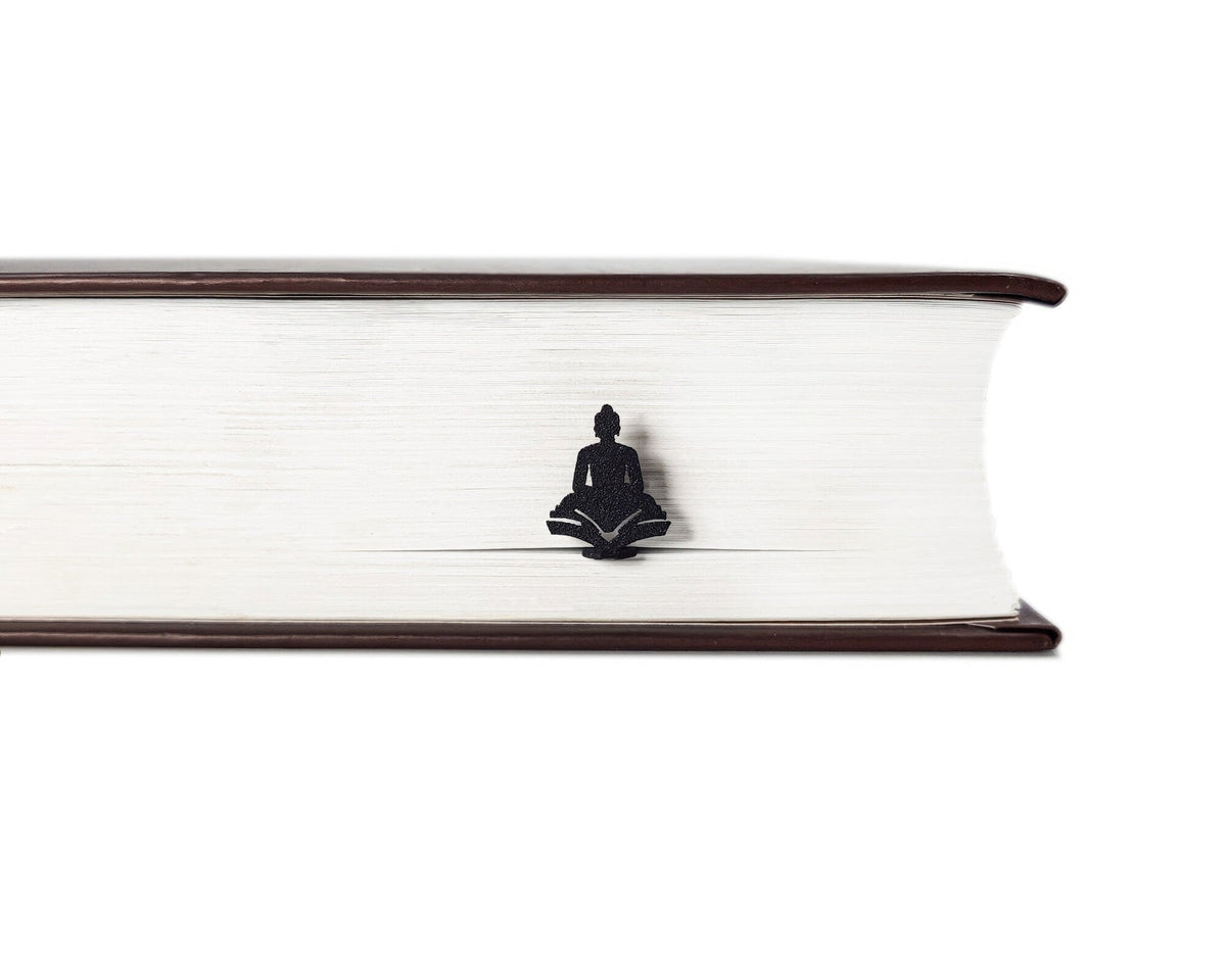 Reading Buddha metal bookmark in a closed book, only its top showing above the pages