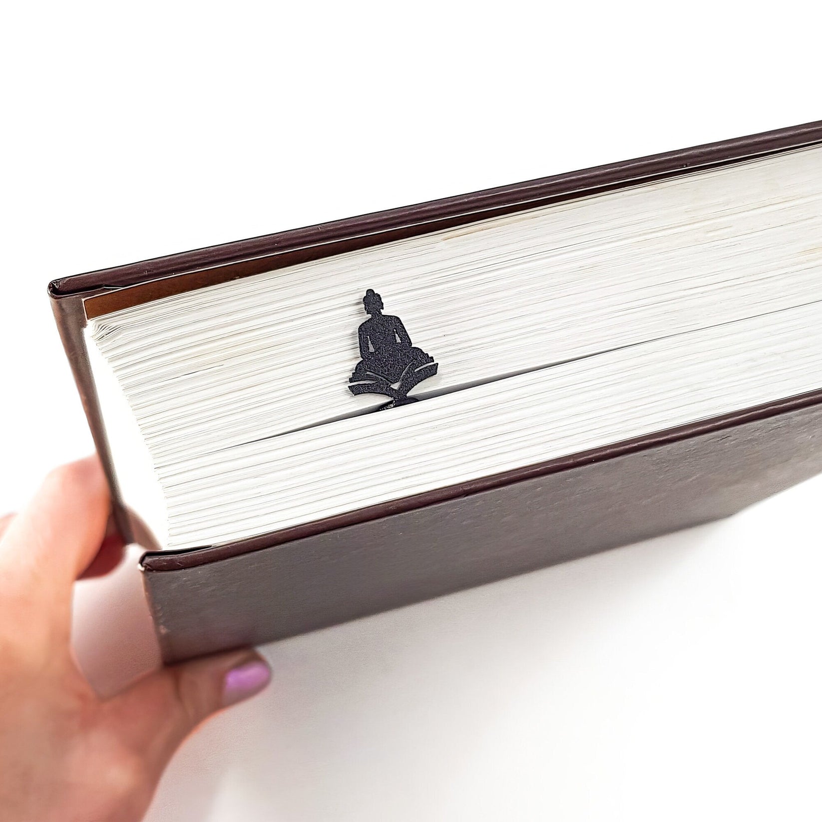 Reading Buddha metal bookmark held in a hand above an open book