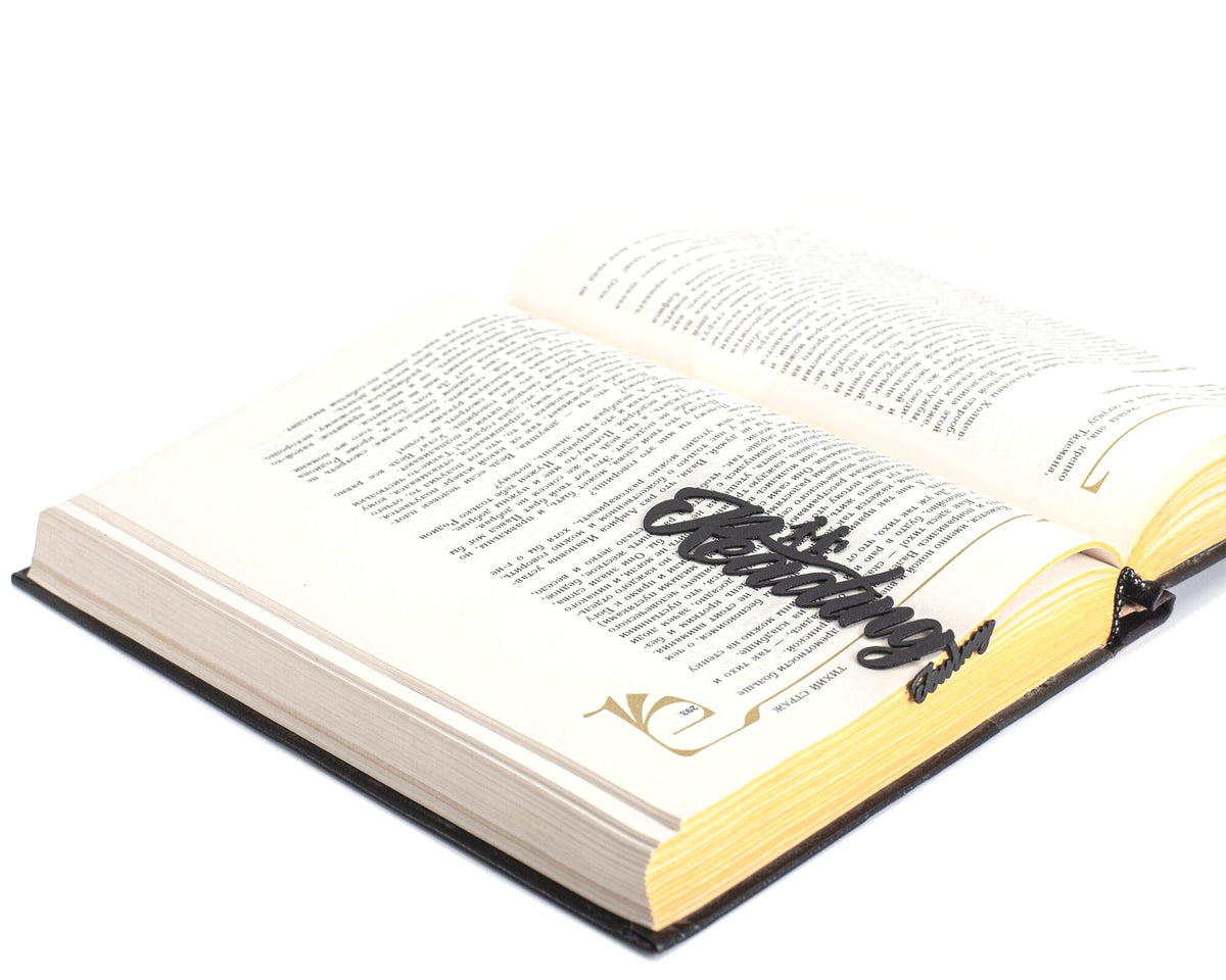Reading Journey metal bookmark marking a page in an open book