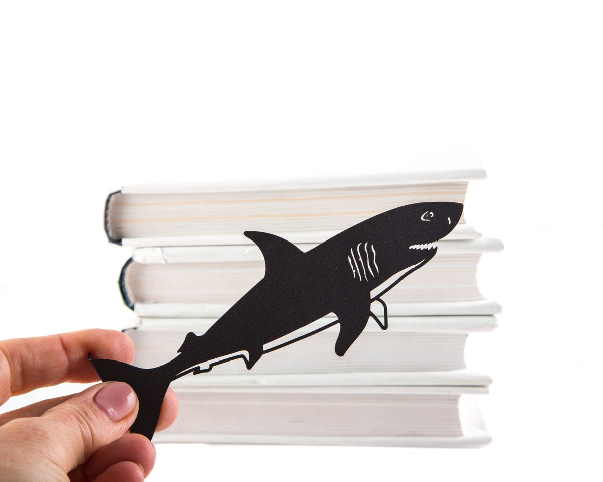 Reading Shark metal bookmark held in a hand above an open book