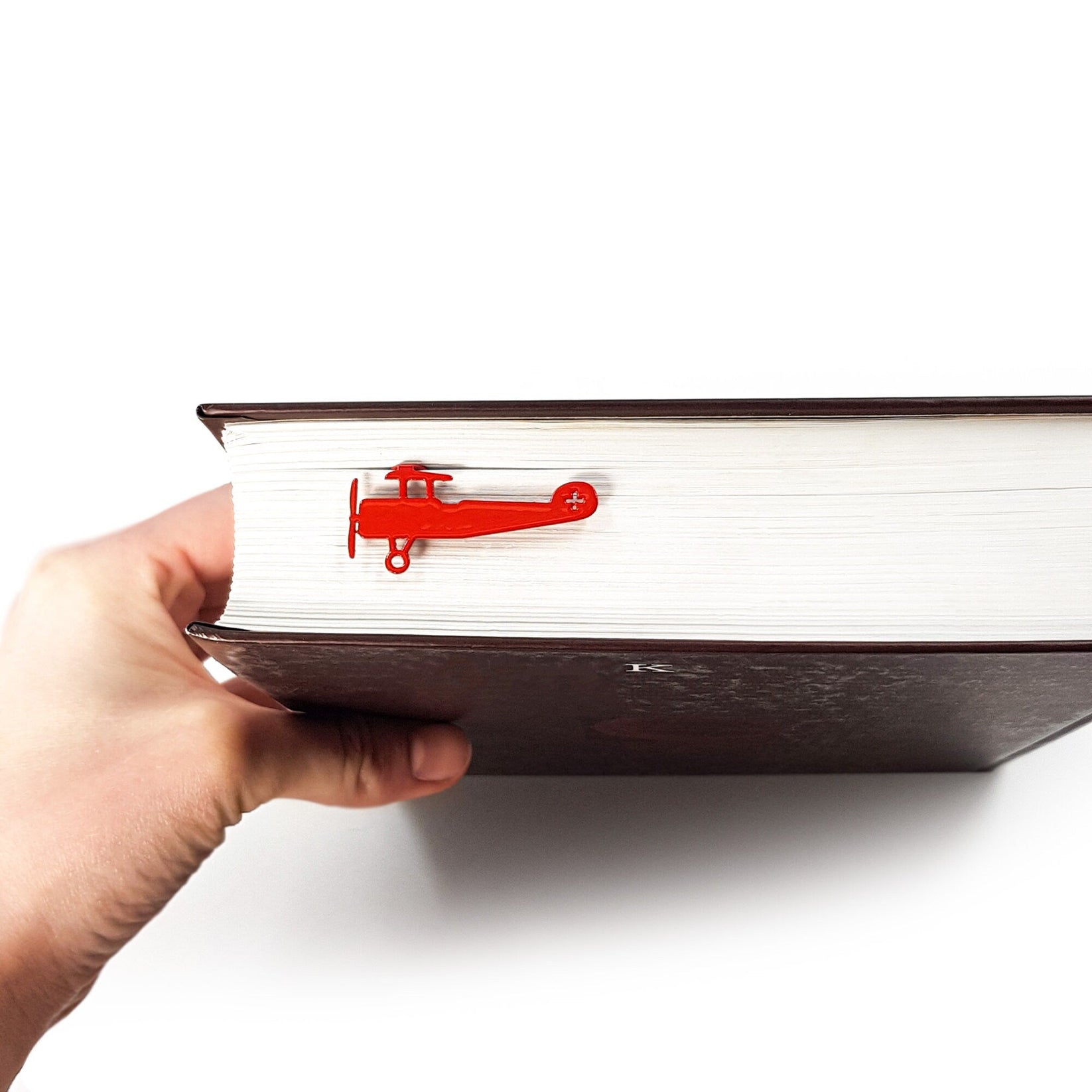 Red Biplane metal bookmark in red held in a hand above an open book
