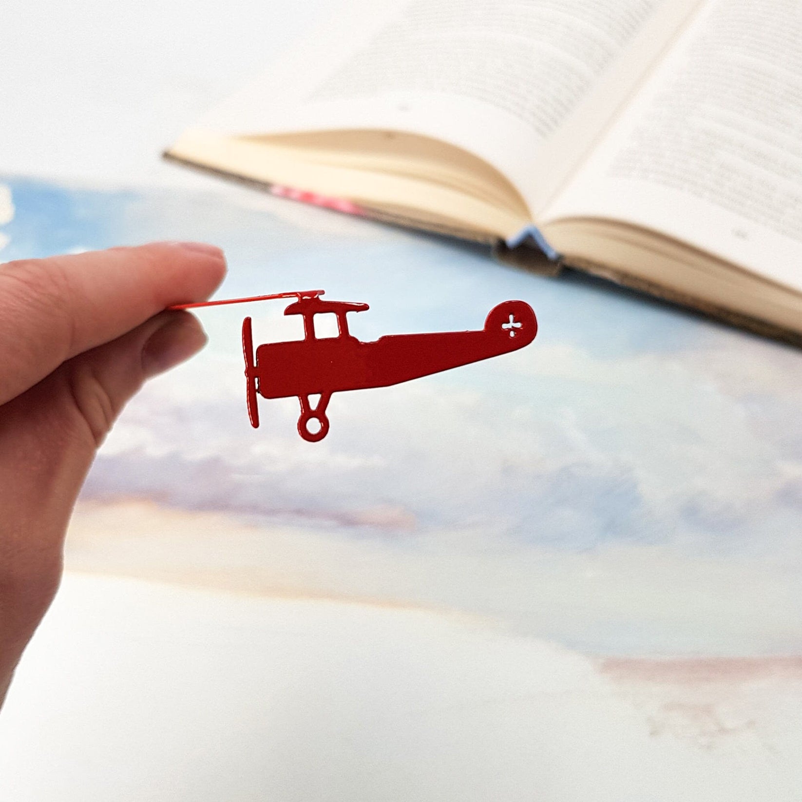 Red Biplane metal bookmark in red held up beside an open book