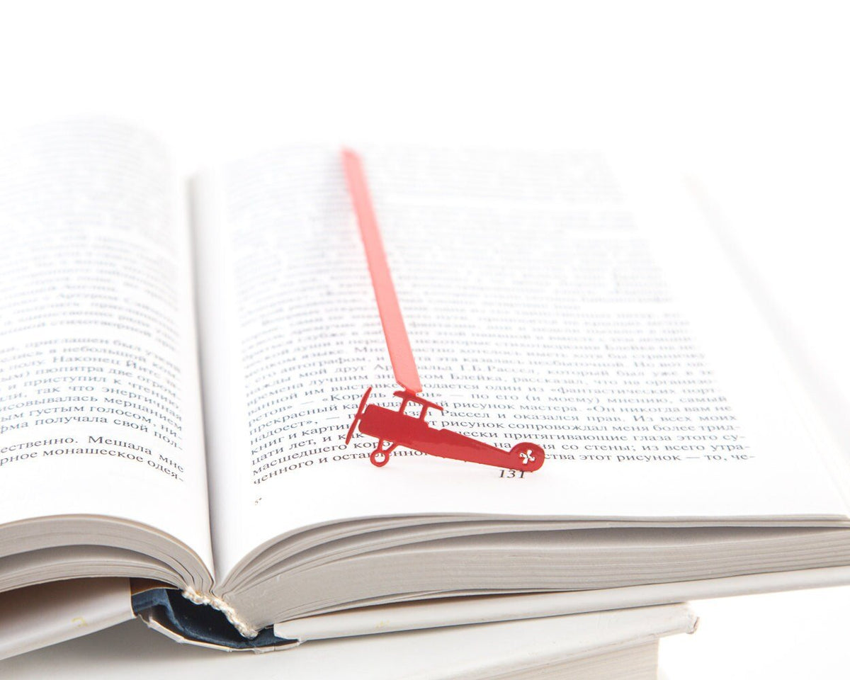 Red Biplane metal bookmark in red resting on the pages of an open book