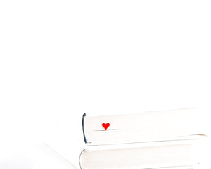 Ace of Hearts metal bookmark in red in a closed book, only its top showing above the pages