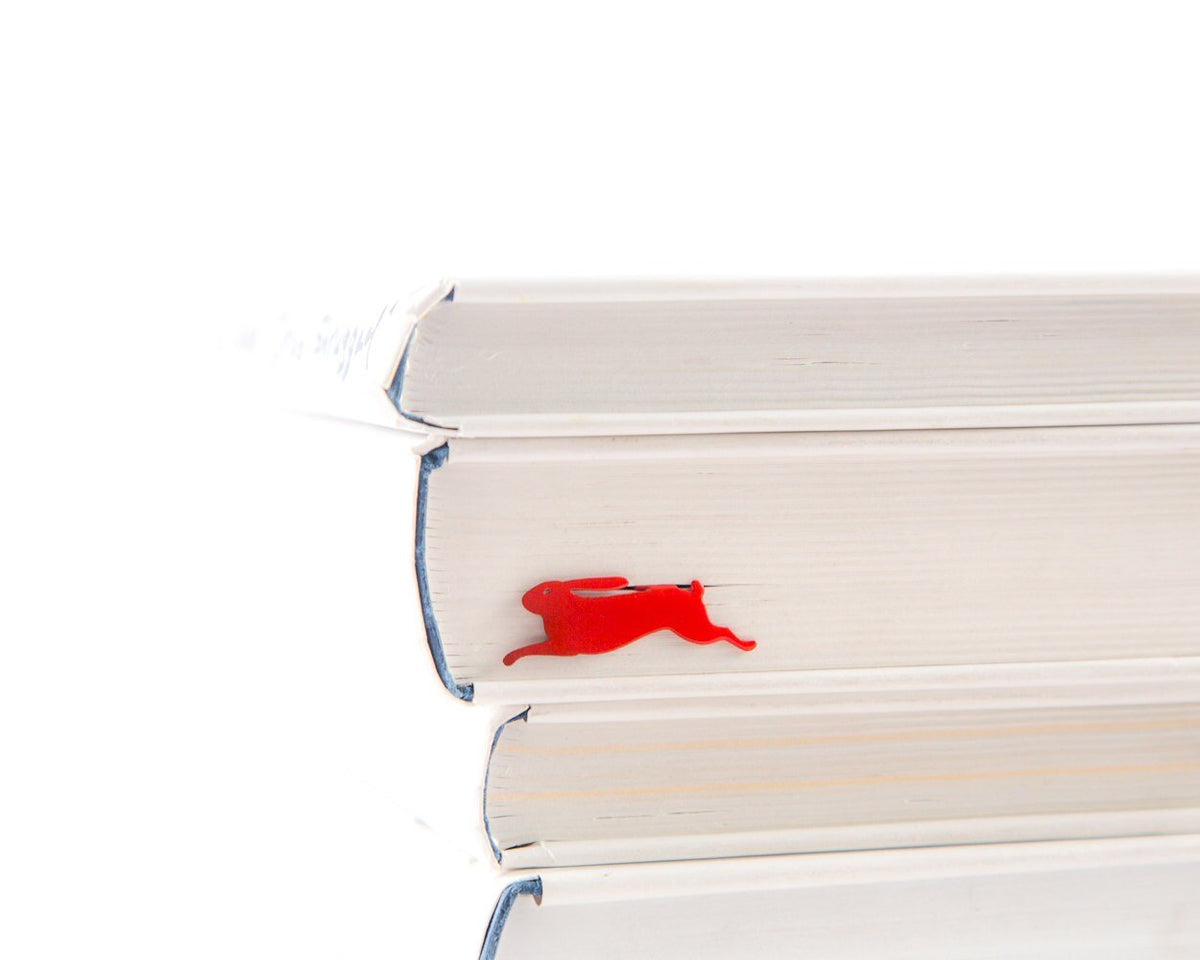 Red Rabbit metal bookmark in red shown with a stack of books