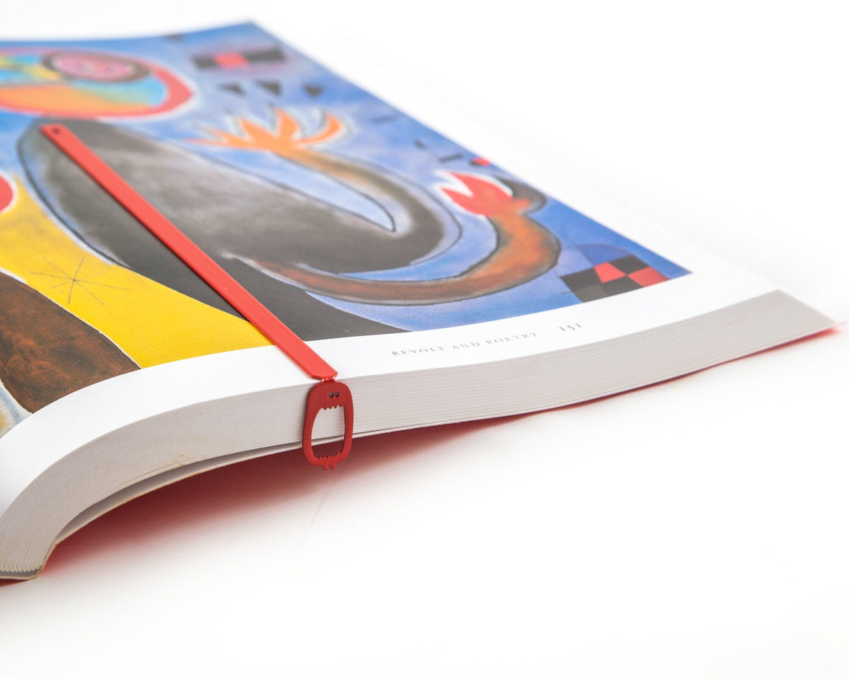 Red Screaming Monster metal bookmark in red marking a page in an illustrated book