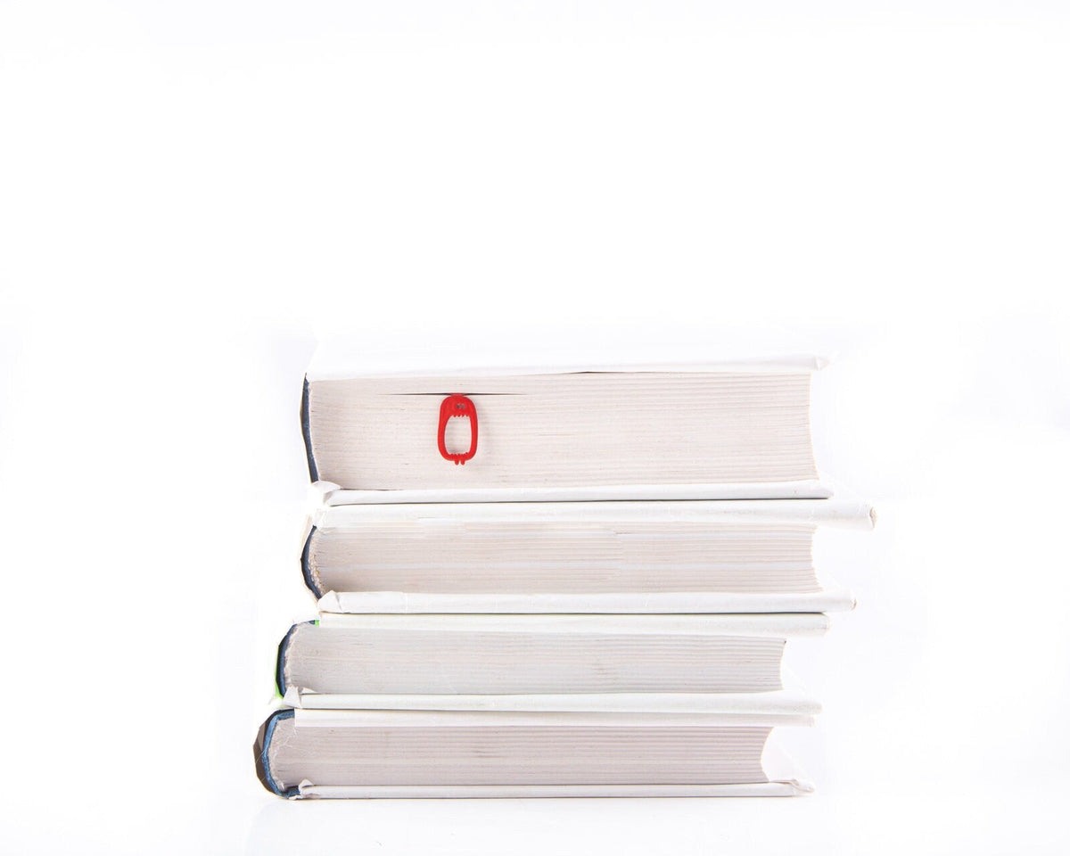 Red Screaming Monster metal bookmark in red shown with a stack of books