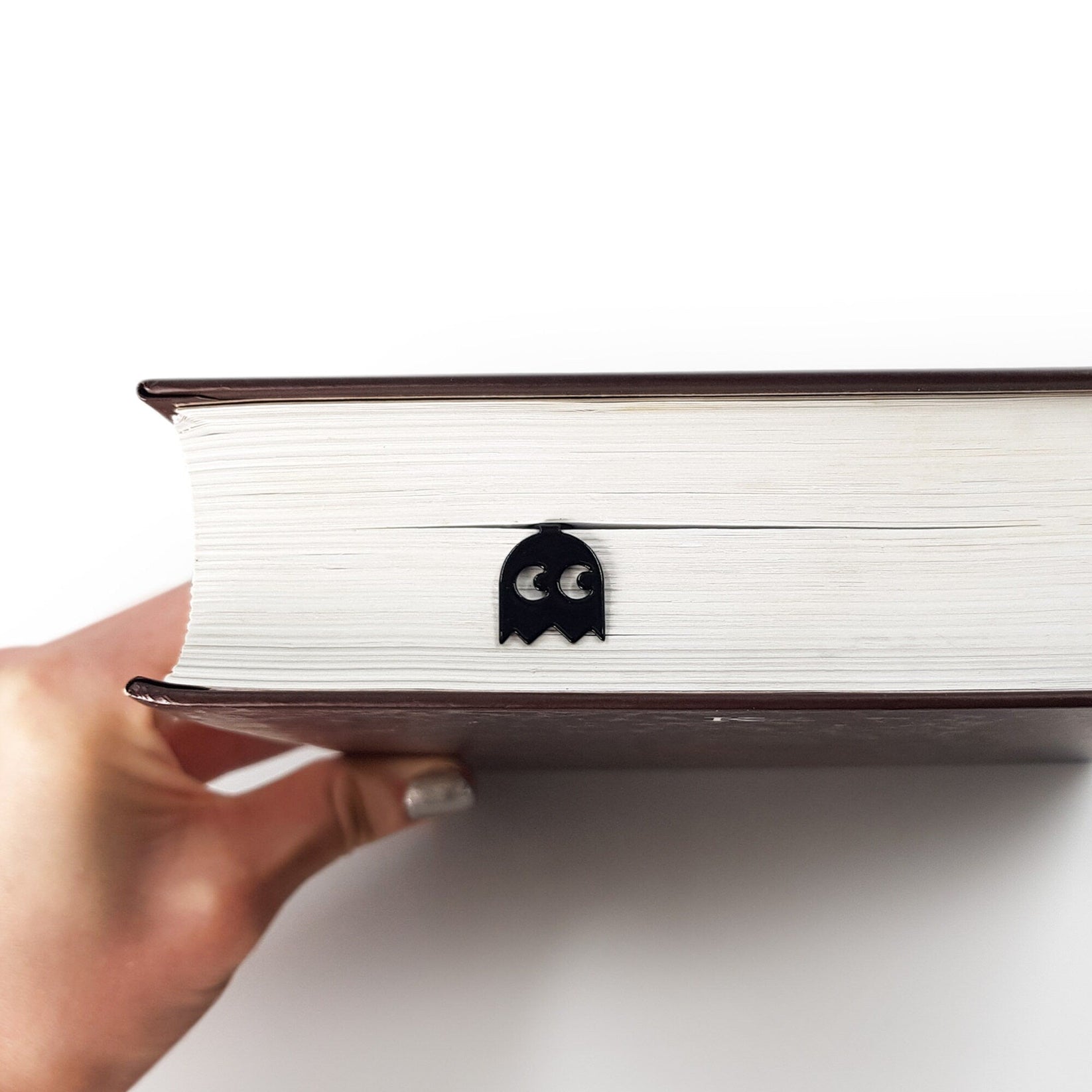 Retro Ghost metal bookmark held up beside an open book