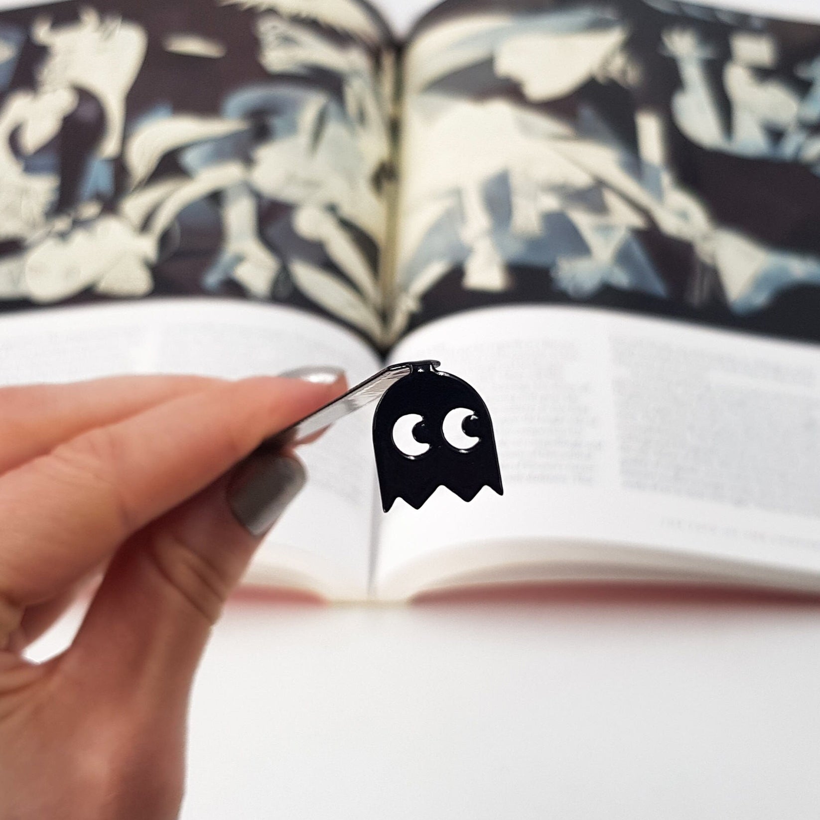 Retro Ghost metal bookmark held in a hand above an open book