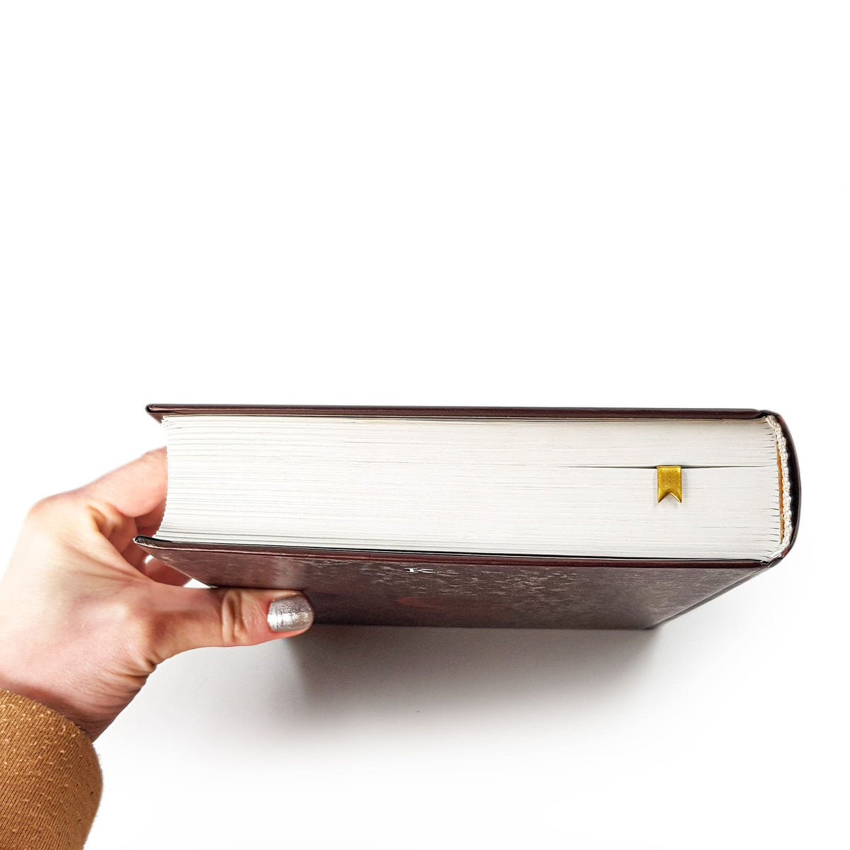 Ribbon metal bookmark in gold held up beside an open book