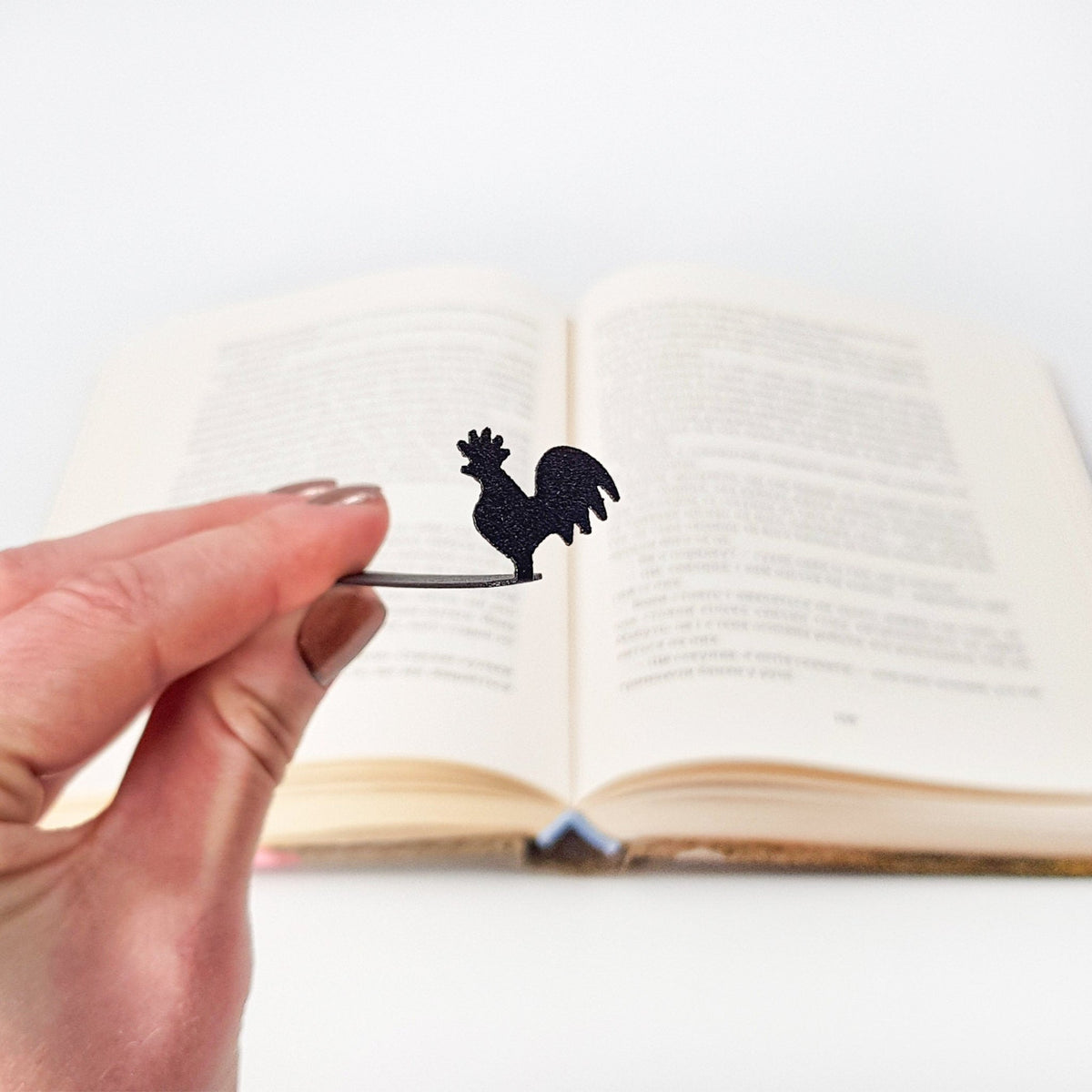 Rooster metal bookmark held in a hand above an open book