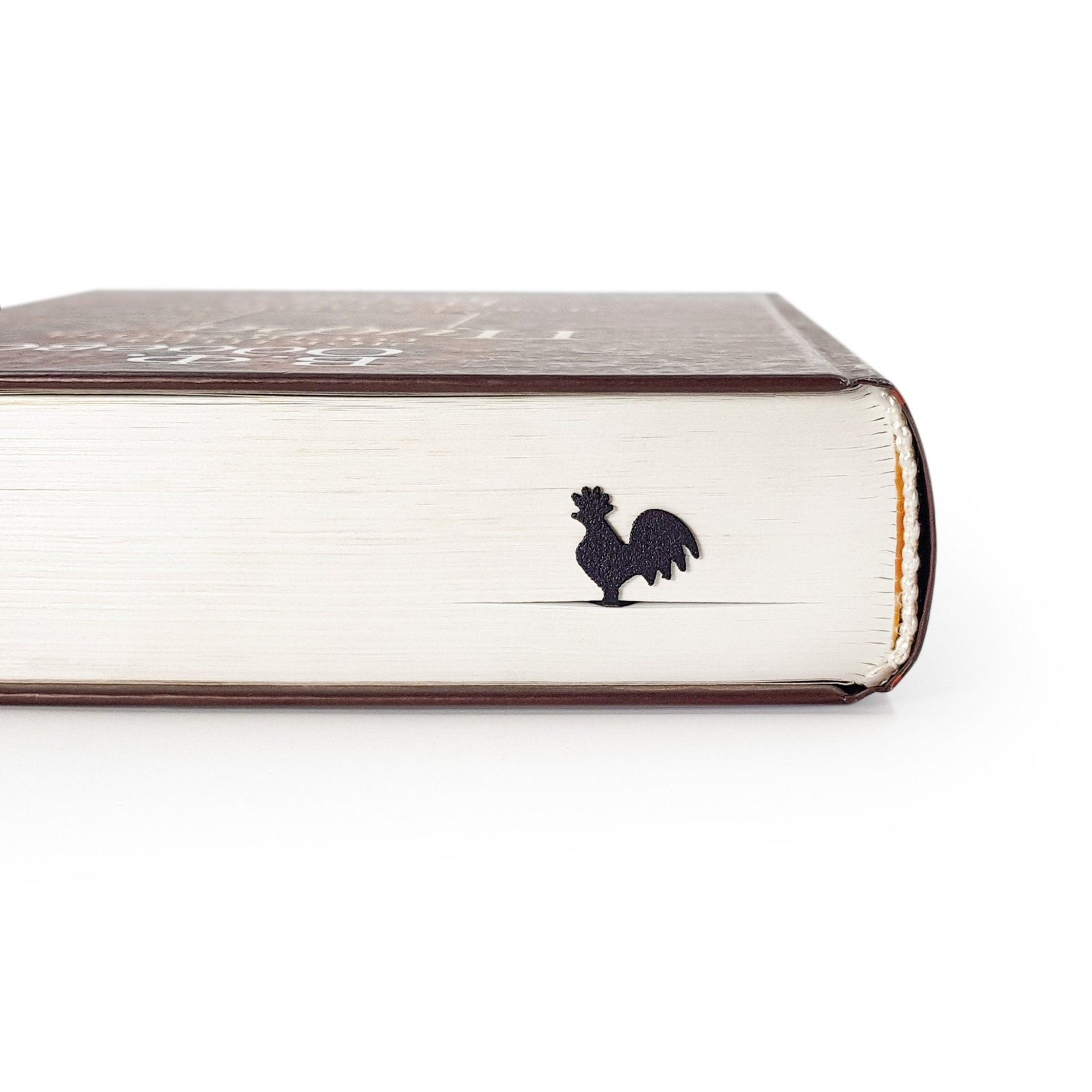 Rooster metal bookmark seen from the edge of a closed book