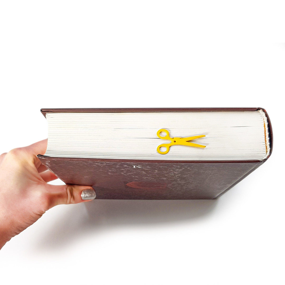 Scissors metal bookmark in gold held in a hand above an open book