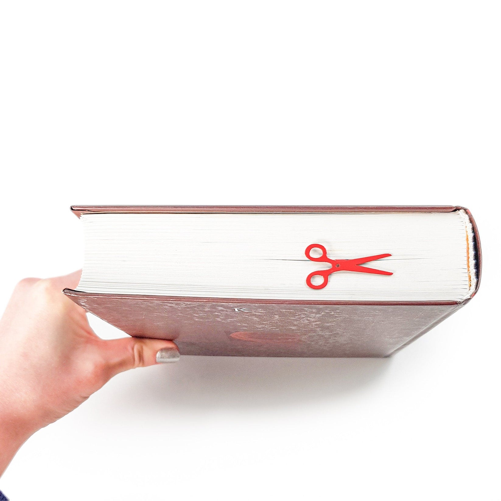 Scissors metal bookmark in red held up beside an open book