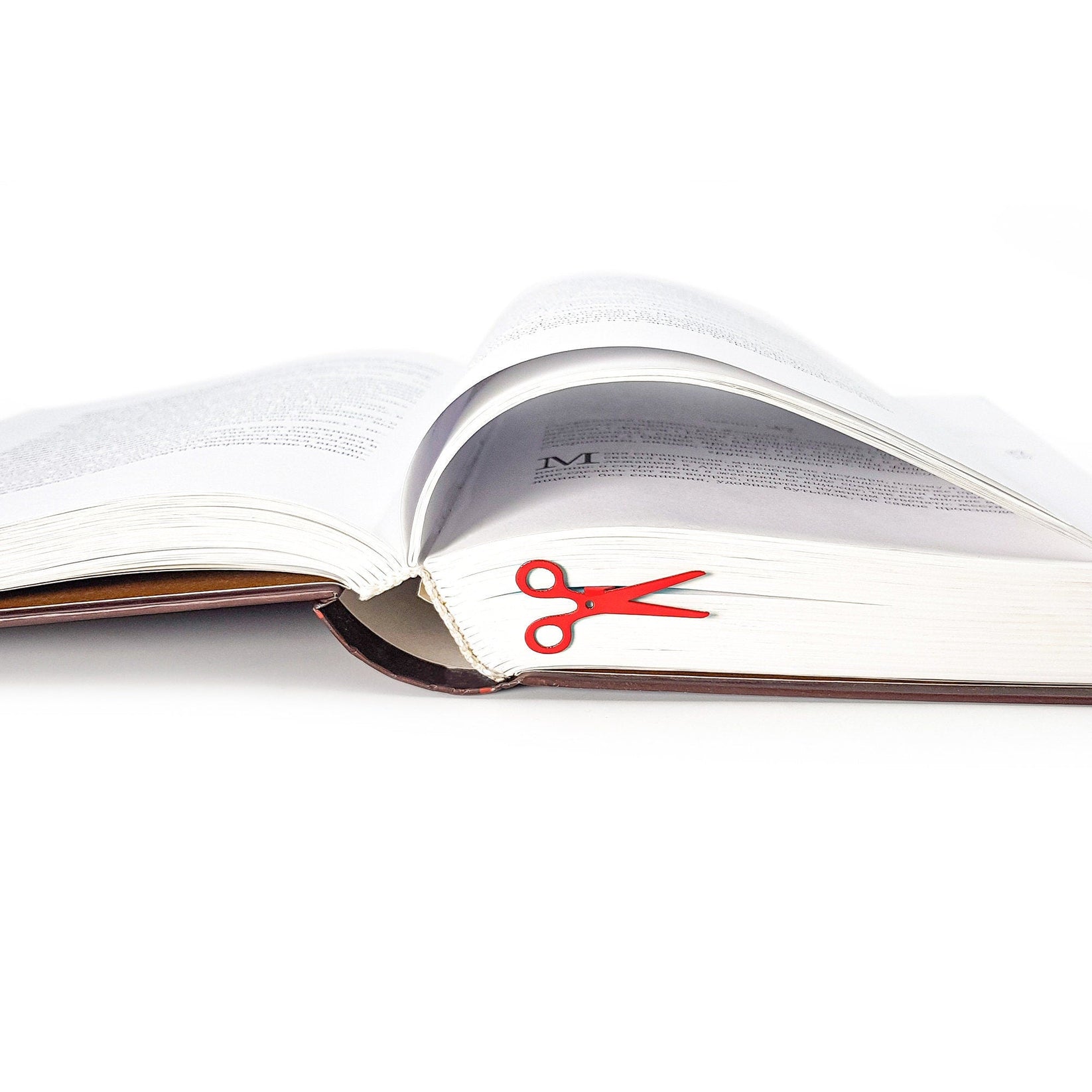 Scissors metal bookmark in red in a closed book, only its top showing above the pages