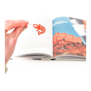 Shrimp metal bookmark in red marking a page in an illustrated book